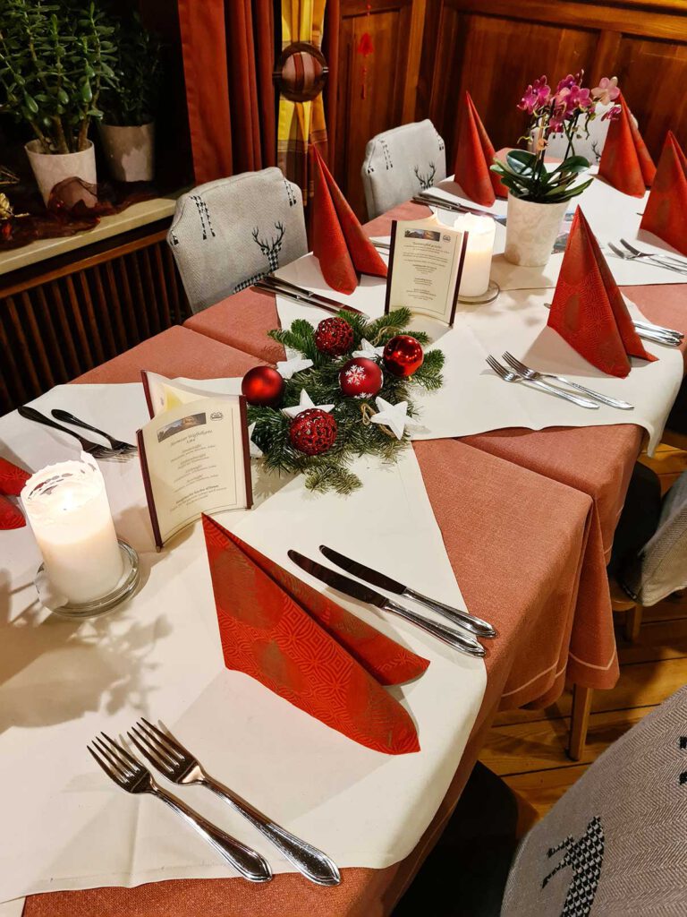 Ein festlich gedeckter Esstisch mit roten Servietten, Menükarten und einem Tafelaufsatz mit roten und silbernen Ornamenten.